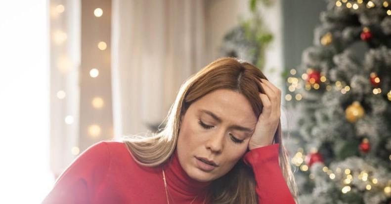 Photo of someone looking stressed by a Christmas tree. 